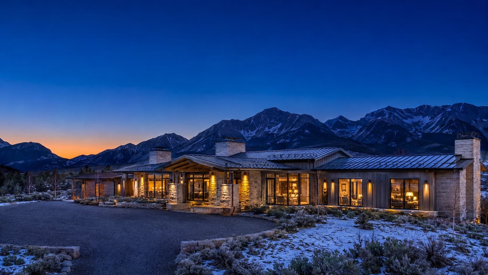 Dusk exterior of a mountain-modern estate above Aspen with warm light glowing through floor-to-ceiling glass